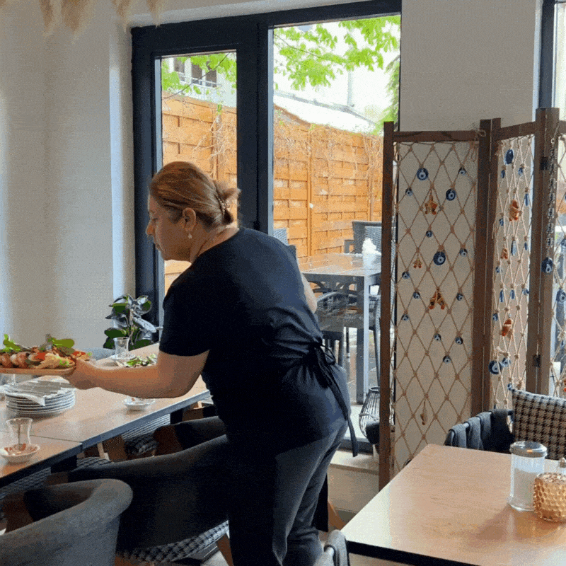 Ein Tisch mit Cay Gläsern, Brot und Tellern der gerade von der Zeyno Inhaberin für das Serpme Frühstück vorbereitet wird. 