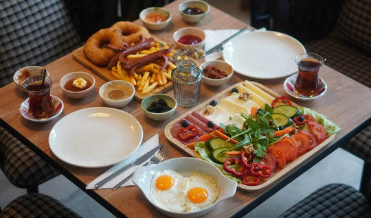 Ein gedeckter Frühstückstisch im Zeyno Café mit verschiedenen Speisen wie Pommes, Würstchen, Käse, Gemüse, Oliven, Spiegeleiern und türkischem Tee. Verschiedene Schälchen mit Soßen und Beilagen umgeben die Teller.