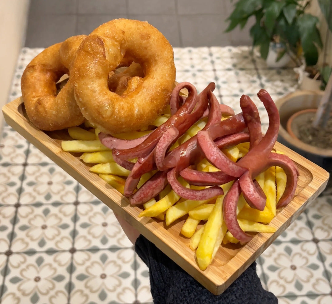 Ein Teller mit Pommes frites, zwei goldbraun frittierten Pişi (türkische "Bagels", ähnlich wie Churros) und aufgeschnittenen Würstchen, die wie kleine Kraken aussehen. Im Hintergrund ist ein gemusterter Fliesenboden zu sehen.