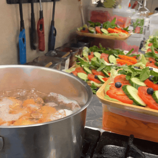 Frische, bunte Salatteller mit Tomaten, Gurken, Paprika, Salatblättern und Blaubeeren, die im Zeyno Restaurant vorbereitet werden. Im Vordergrund ist ein Topf zu sehen, in dem Eier kochen.